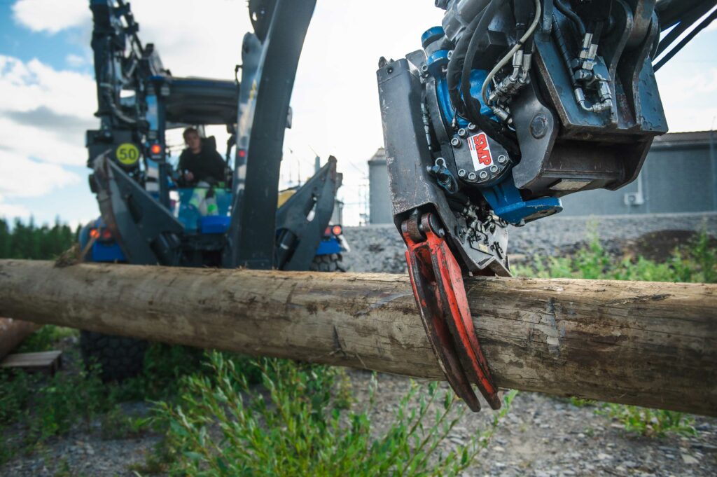 Woman in an excavator and a ripper bucket doing work on a log