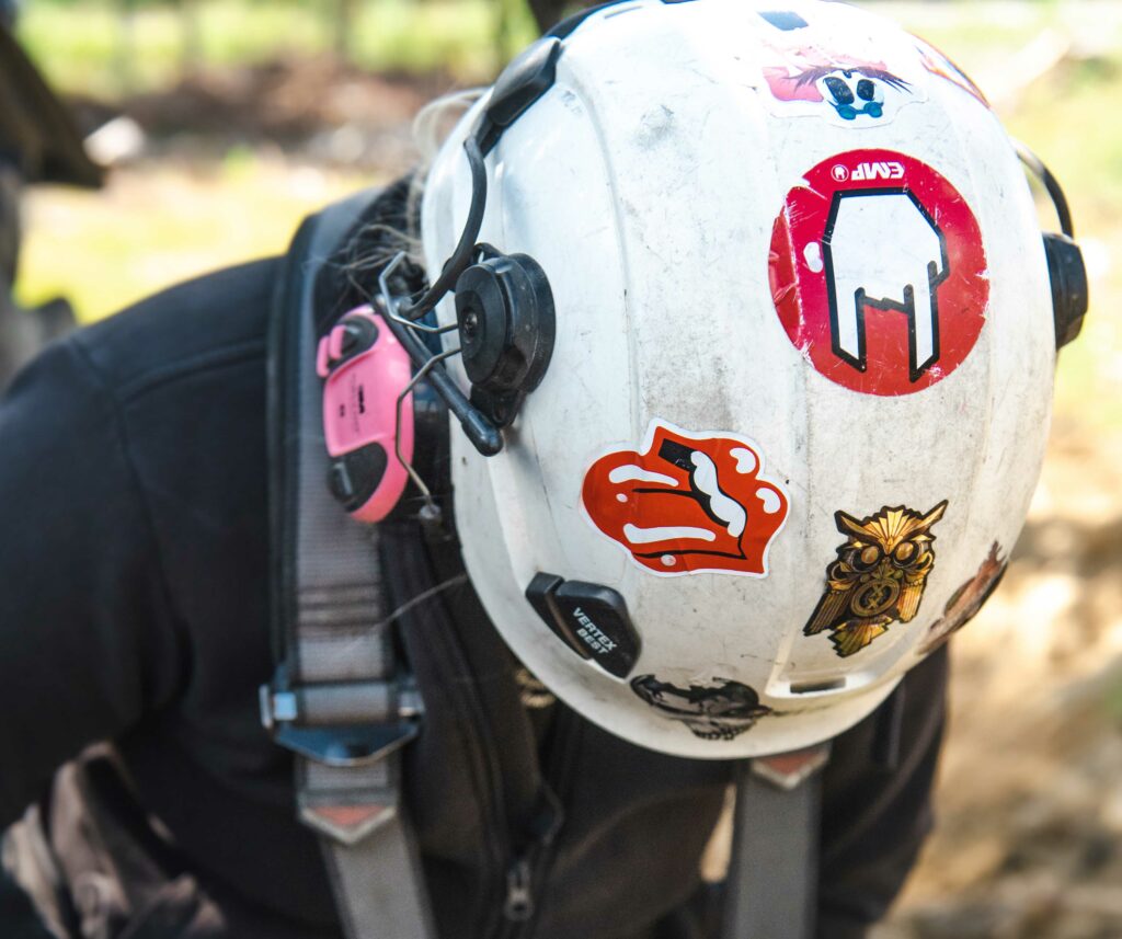 Person wearing a white hard hat with lots of stickers and a safety harness