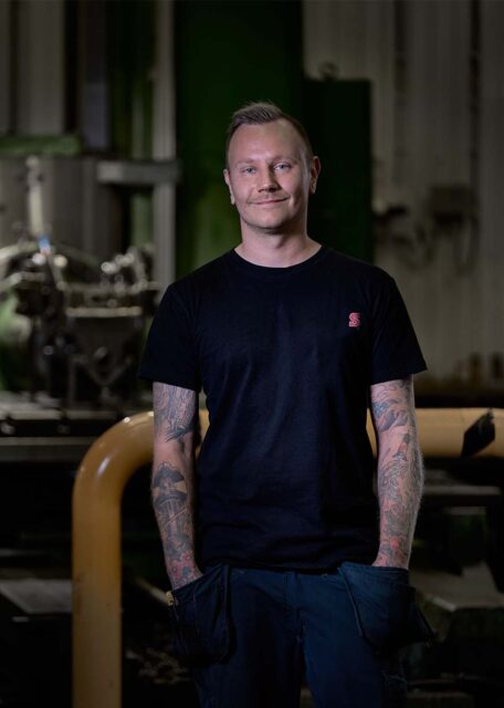 Man in SMP parts production facility with tattoos and smiling