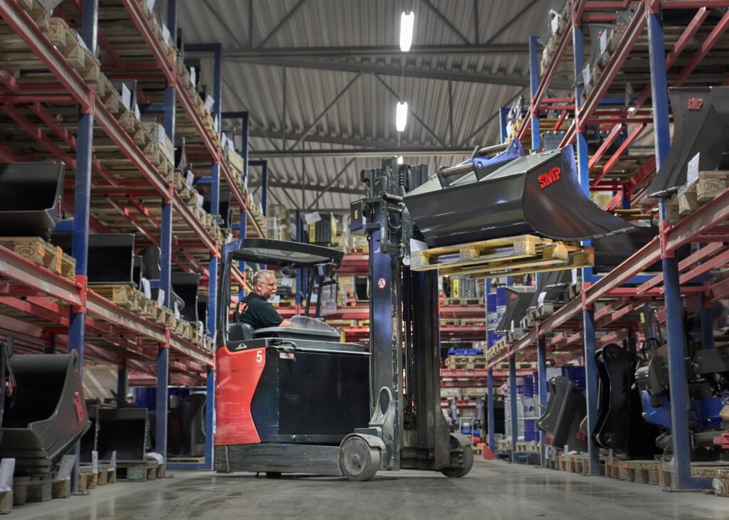 Man driving a forklift and grabbing a SMP excavator bucket on the shelf