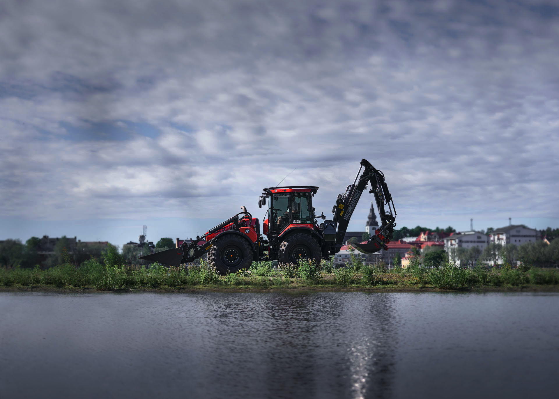 Red excavator with two buckets in Sweden next to a lake