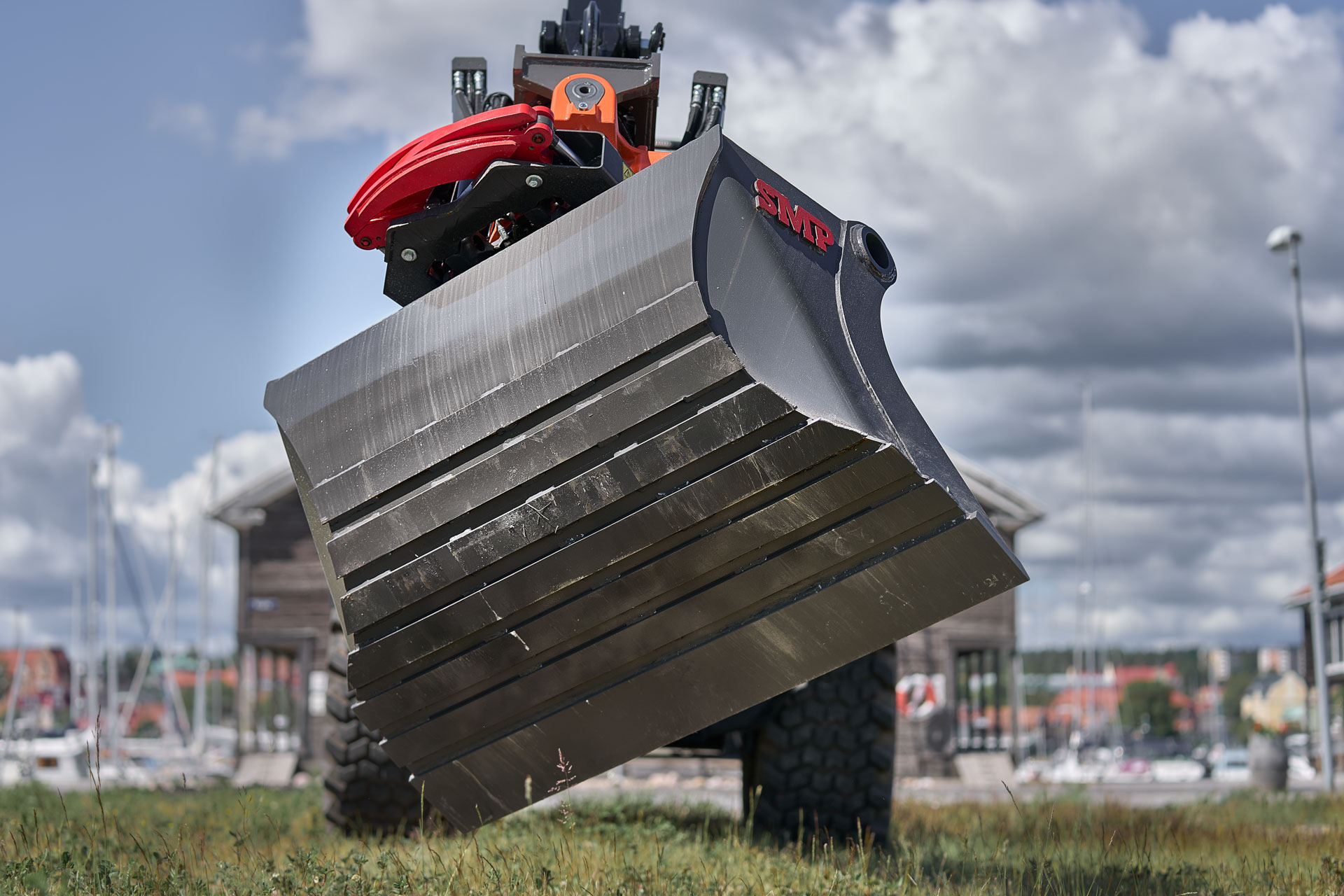 Closeup of an SMP bucket with a tiltrotator attached in front of a marina in Sweden