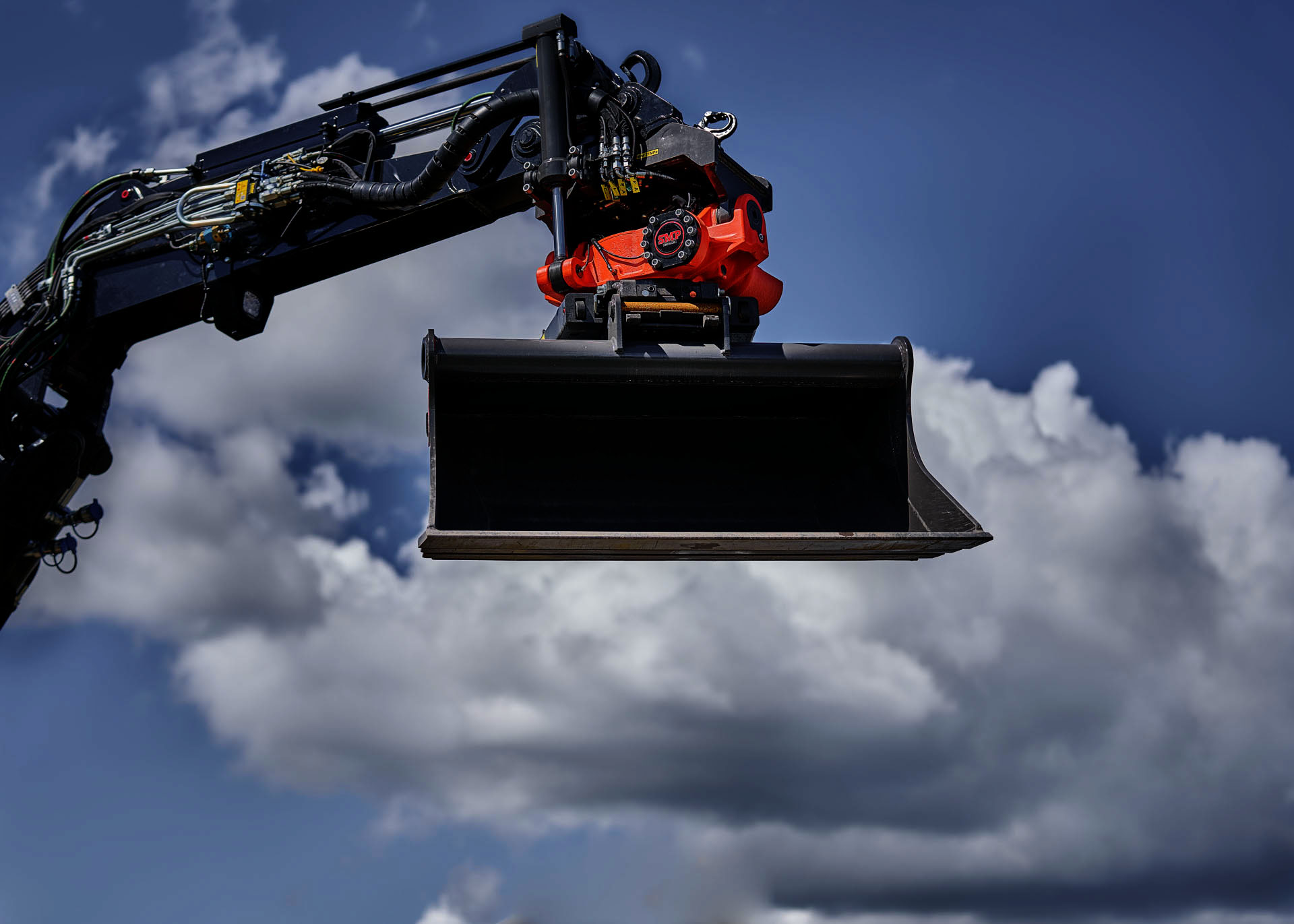 SMP Parts excavator bucket with a quick coupler and tiltrotator in the air in front of clouds