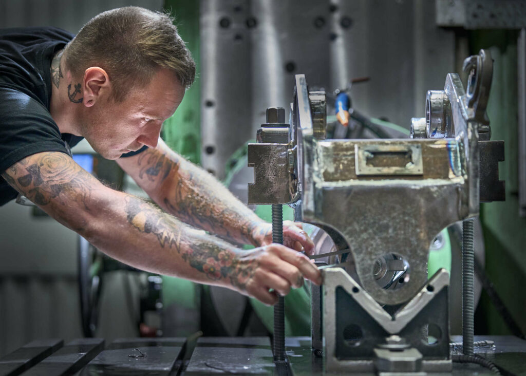 Man with tattoos making holes with a drill in to a quick coupler for excavators